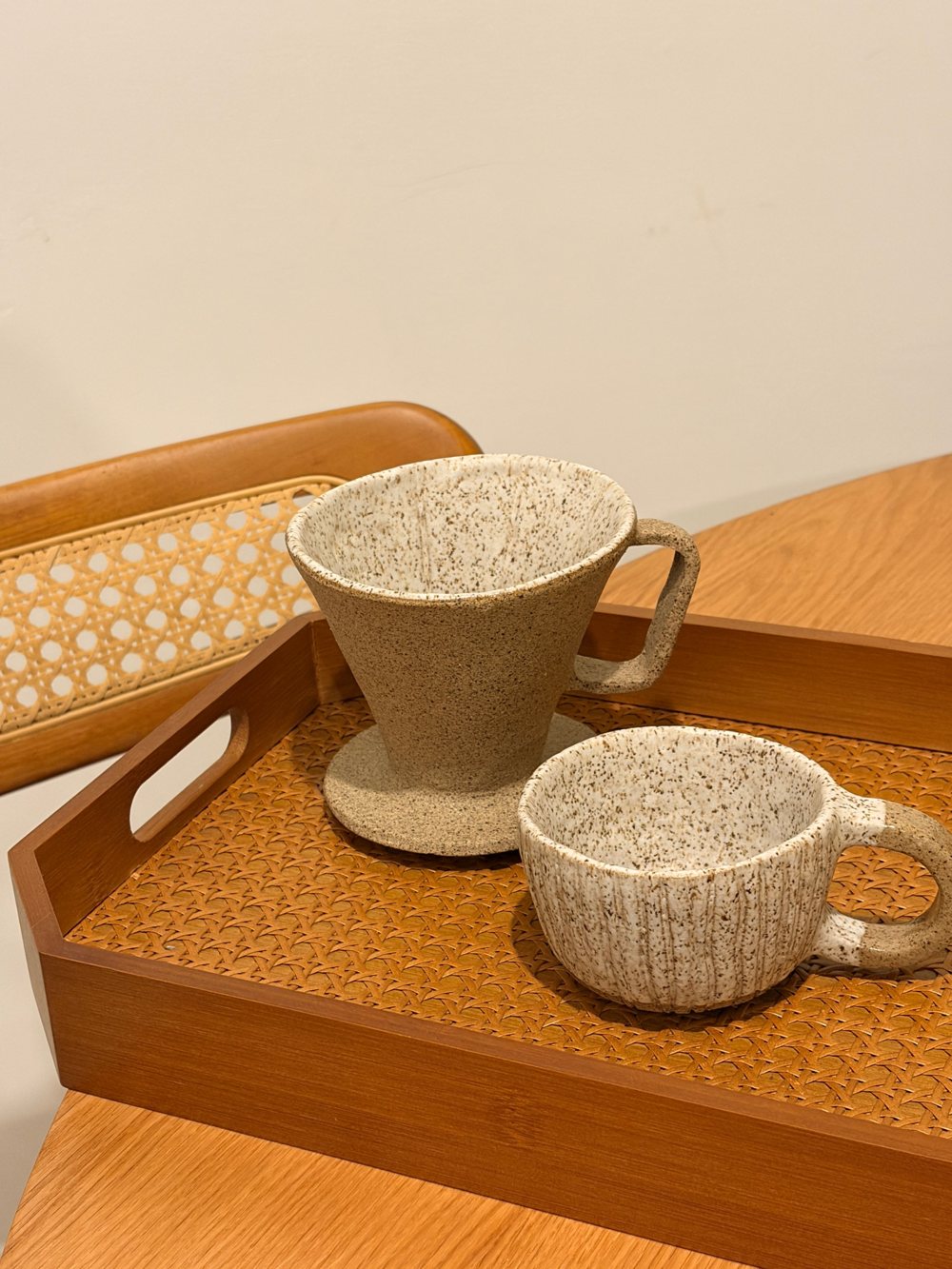 Coador e caneca de cerâmica com esmalte salpicado sobre uma bandeja de palhinha